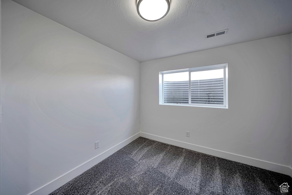Empty room featuring baseboards, dark colored carpet, and a textured ceiling