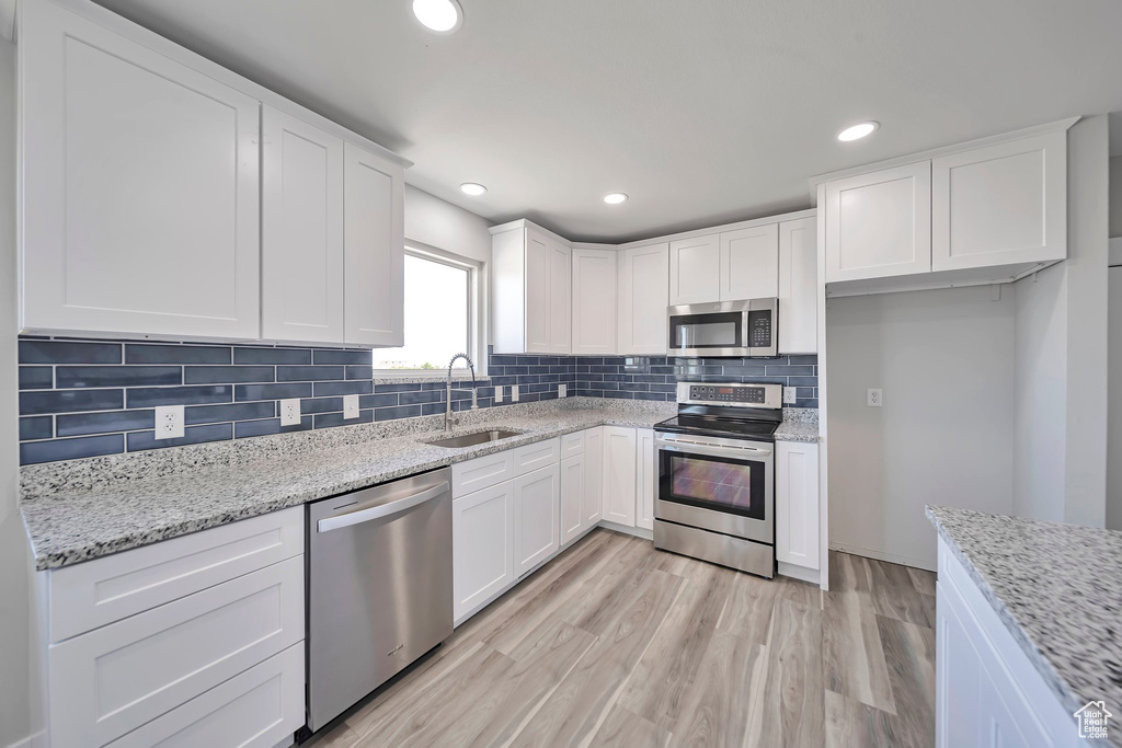 Kitchen featuring appliances with stainless steel finishes, a sink, white cabinets, tasteful backsplash, and light wood finished floors