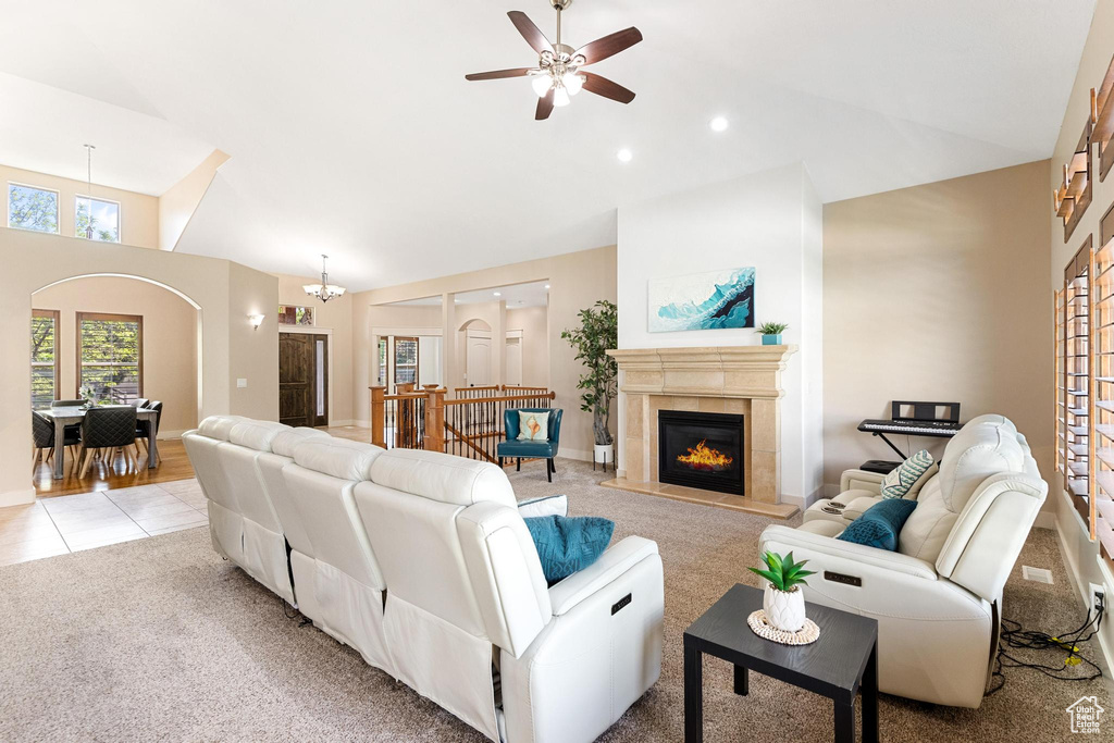 Living area featuring a ceiling fan, a glass covered fireplace, light carpet, high vaulted ceiling, and baseboards