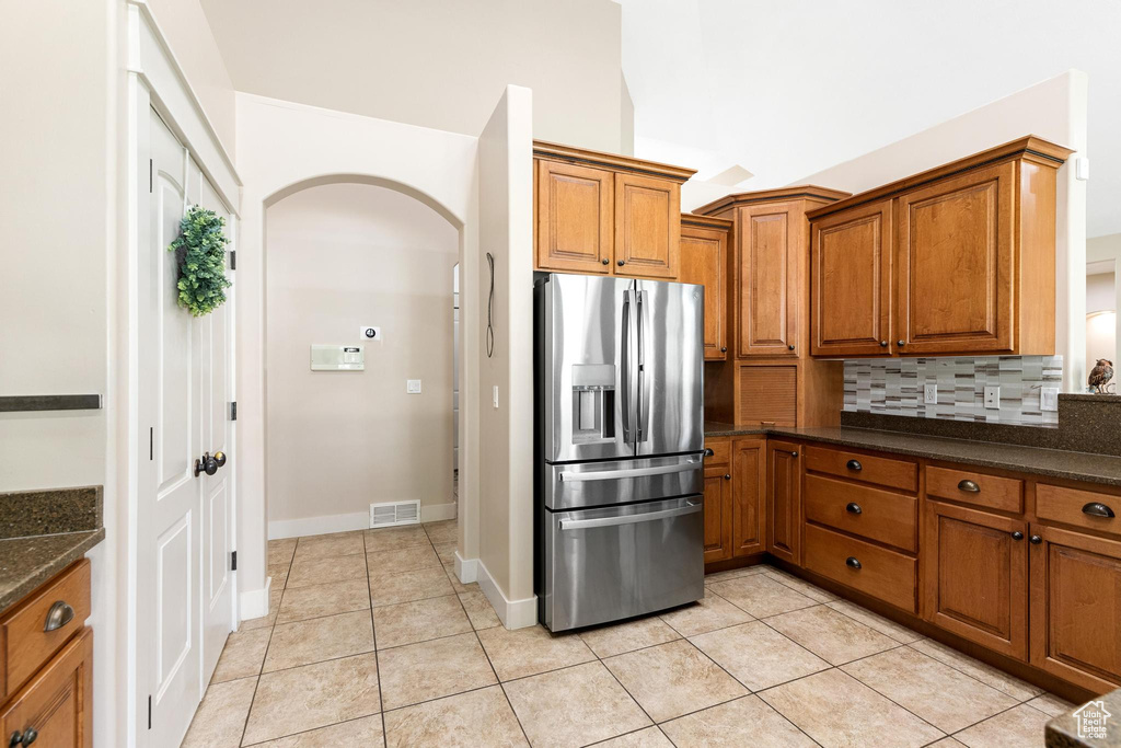 Kitchen with stainless steel fridge with ice dispenser, arched walkways, brown cabinetry, decorative backsplash, and light tile patterned flooring