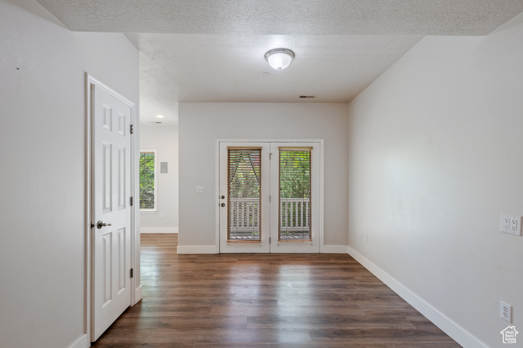 Unfurnished room featuring dark wood-type flooring, baseboards, a textured ceiling, and french doors