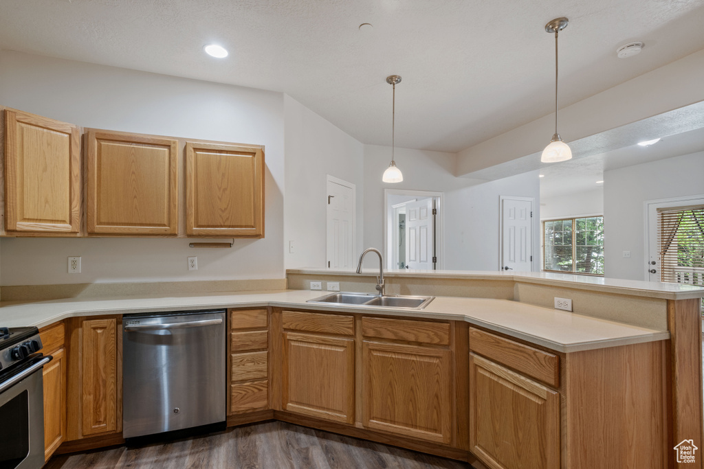 Kitchen with stainless steel appliances, a sink, dark wood finished floors, a peninsula, and light countertops
