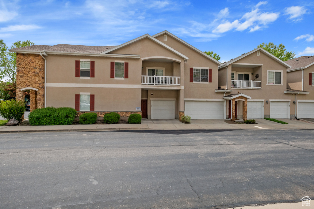 Townhome / multi-family property featuring stone siding, an attached garage, stucco siding, a balcony, and driveway