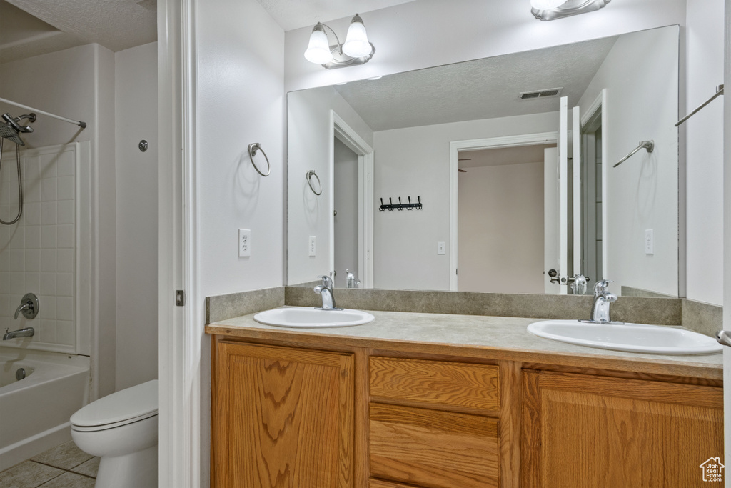 Bathroom with tile patterned floors, toilet, double vanity, and shower / washtub combination