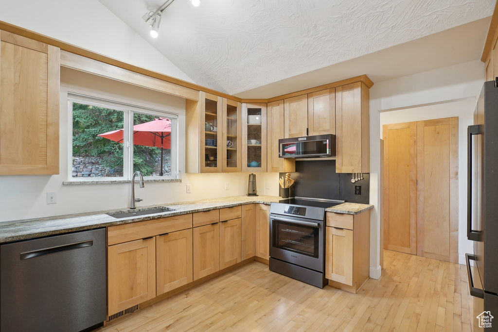 Kitchen with stainless steel appliances, a sink, light brown cabinets, light wood-style floors, and light stone countertops