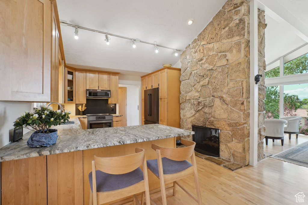 Kitchen featuring stainless steel microwave, high end black fridge, stove, light brown cabinets, and light wood-type flooring