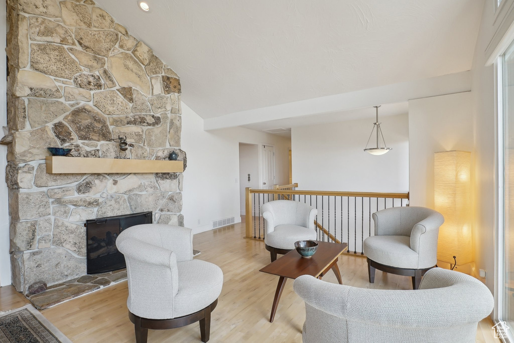Sitting room with wood finished floors, lofted ceiling, and a stone fireplace