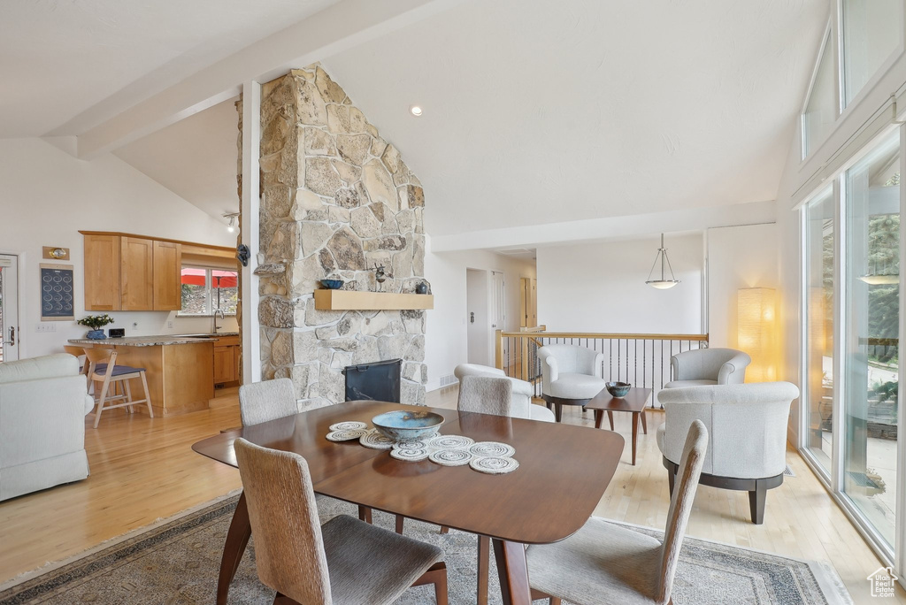 Dining room with healthy amount of natural light, high vaulted ceiling, beam ceiling, a fireplace, and light wood finished floors