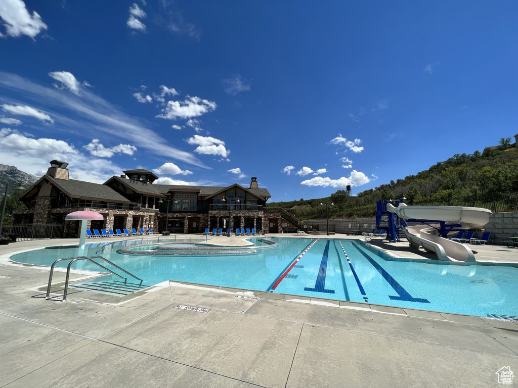 Community pool with a water slide, a patio area, and fence