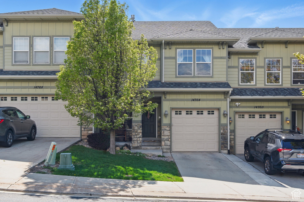 Townhome / multi-family property with board and batten siding, driveway, a garage, and stone siding