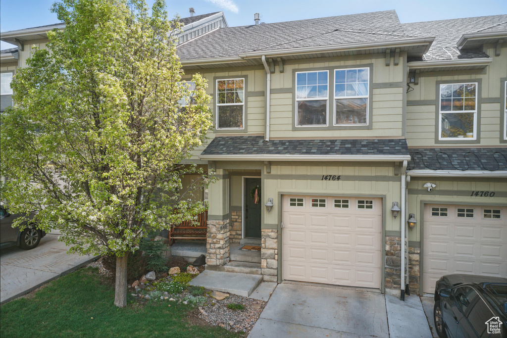 View of property with an attached garage, driveway, stone siding, and a high end roof