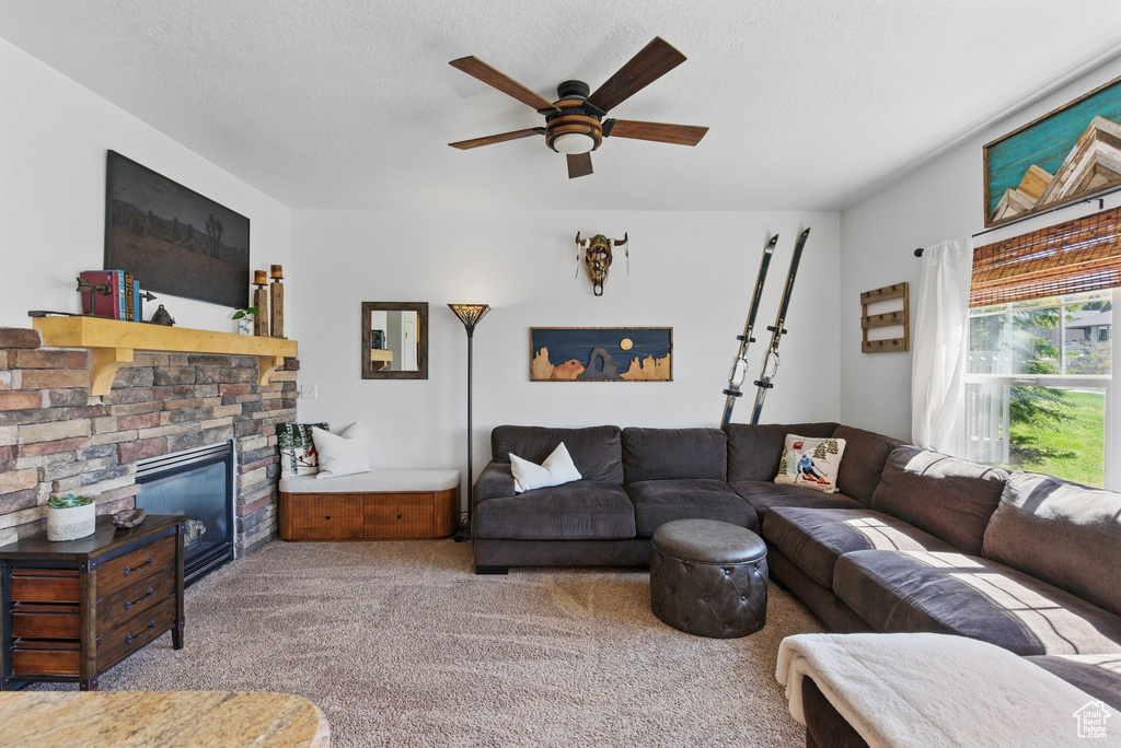 Living room featuring carpet floors, ceiling fan, and a stone fireplace