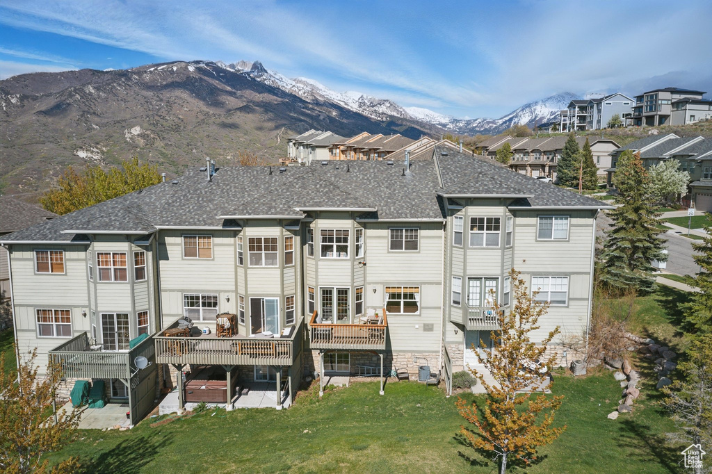 Back of house with a yard, a patio, a deck with mountain view, and roof with shingles