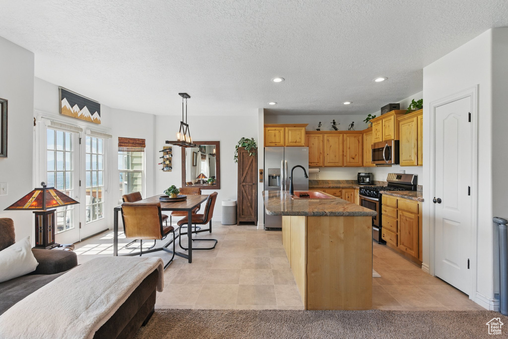Kitchen featuring appliances with stainless steel finishes, a sink, dark stone counters, recessed lighting, and a kitchen island with sink