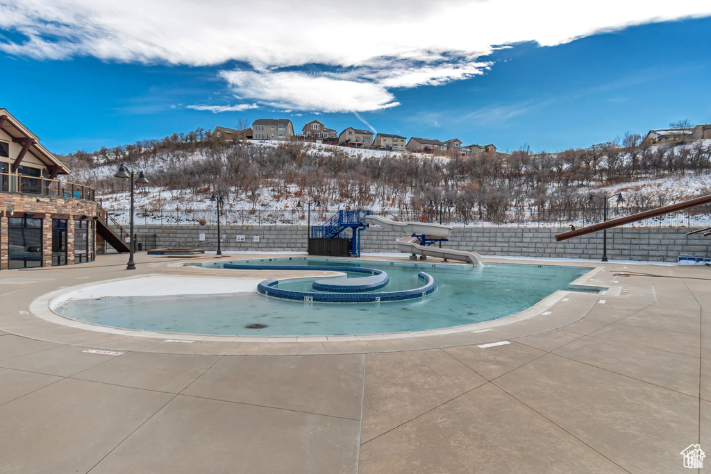 Snow covered pool featuring a water slide, fence, and a hot tub