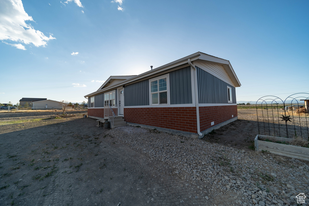 View of front facade featuring brick siding, entry steps, board and batten siding, driveway, and a vegetable garden