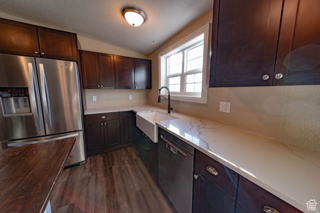 Kitchen with stainless steel appliances, a sink, dark wood-style floors, vaulted ceiling, and light stone counters