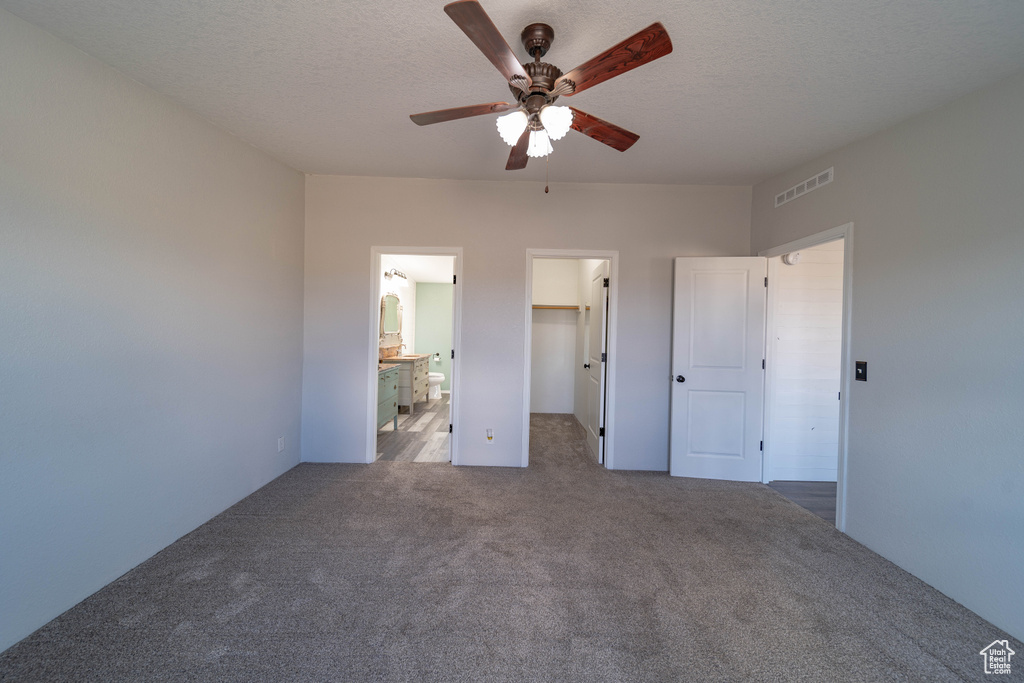 Unfurnished bedroom featuring carpet, a walk in closet, a ceiling fan, a closet, and ensuite bathroom