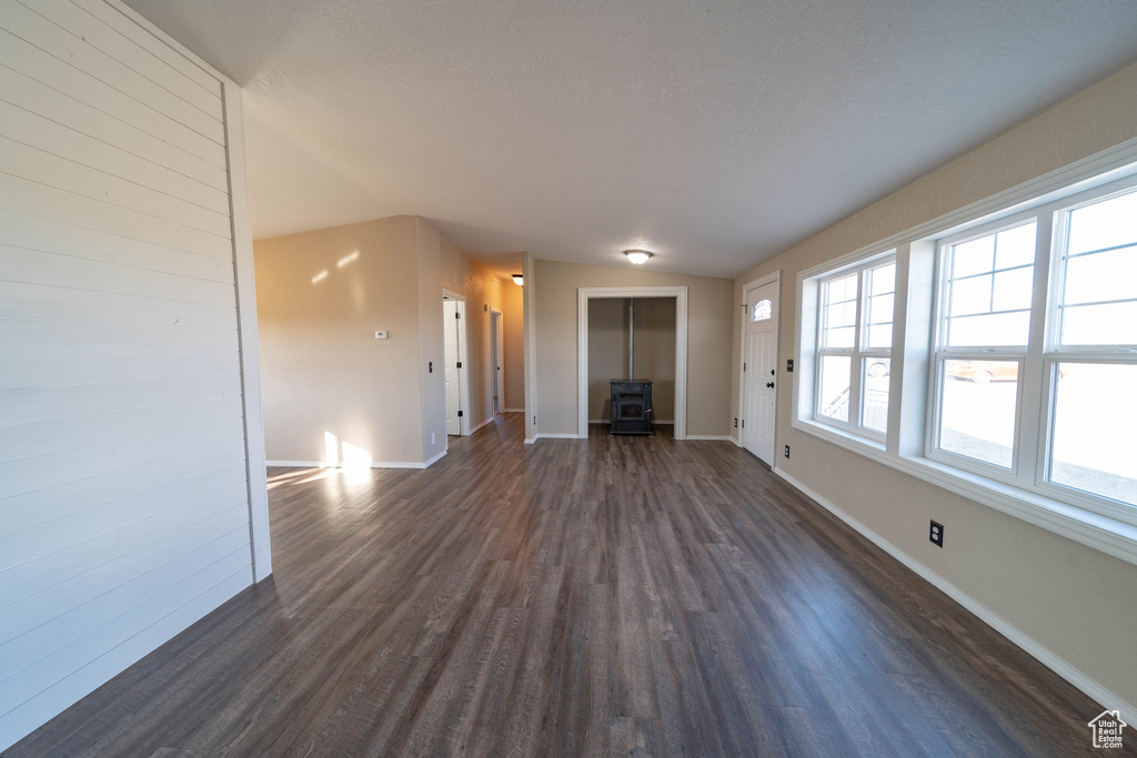 Unfurnished living room featuring dark wood-type flooring, baseboards, and a wood stove
