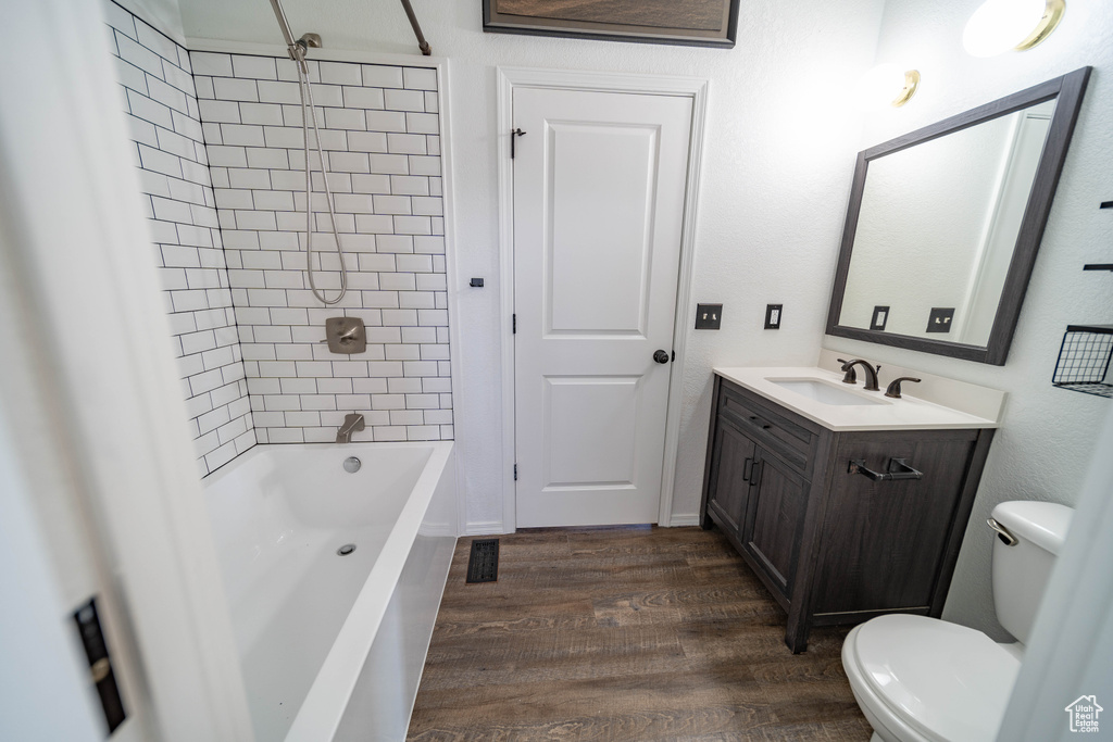 Bathroom with toilet, vanity, wood finished floors, and washtub / shower combination
