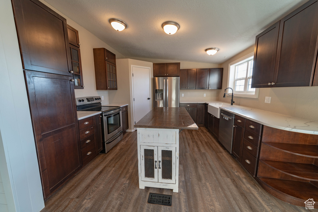 Kitchen featuring appliances with stainless steel finishes, dark wood-style floors, glass insert cabinets, a sink, and dark brown cabinetry