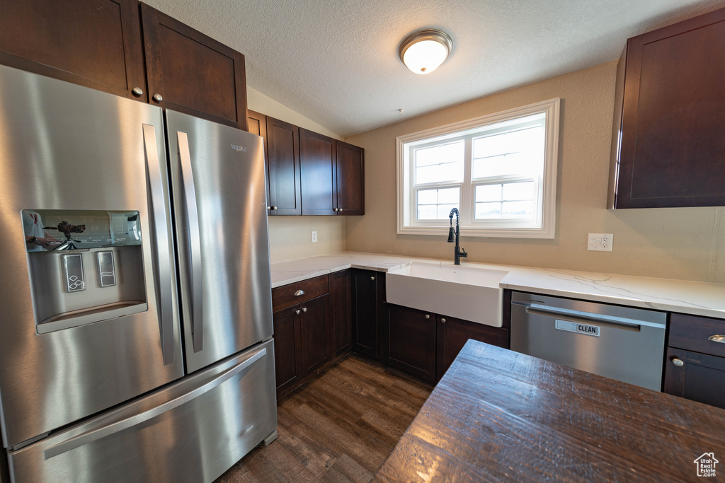 Kitchen featuring appliances with stainless steel finishes, a sink, dark wood-style flooring, dark brown cabinetry, and vaulted ceiling