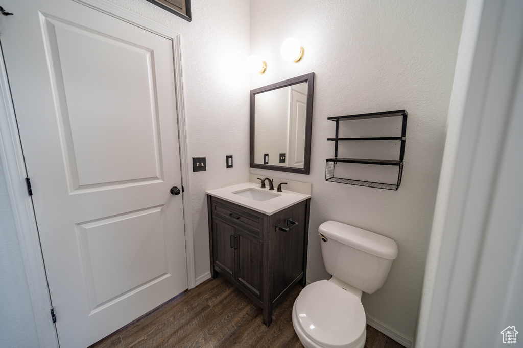 Half bath with vanity, toilet, and wood finished floors