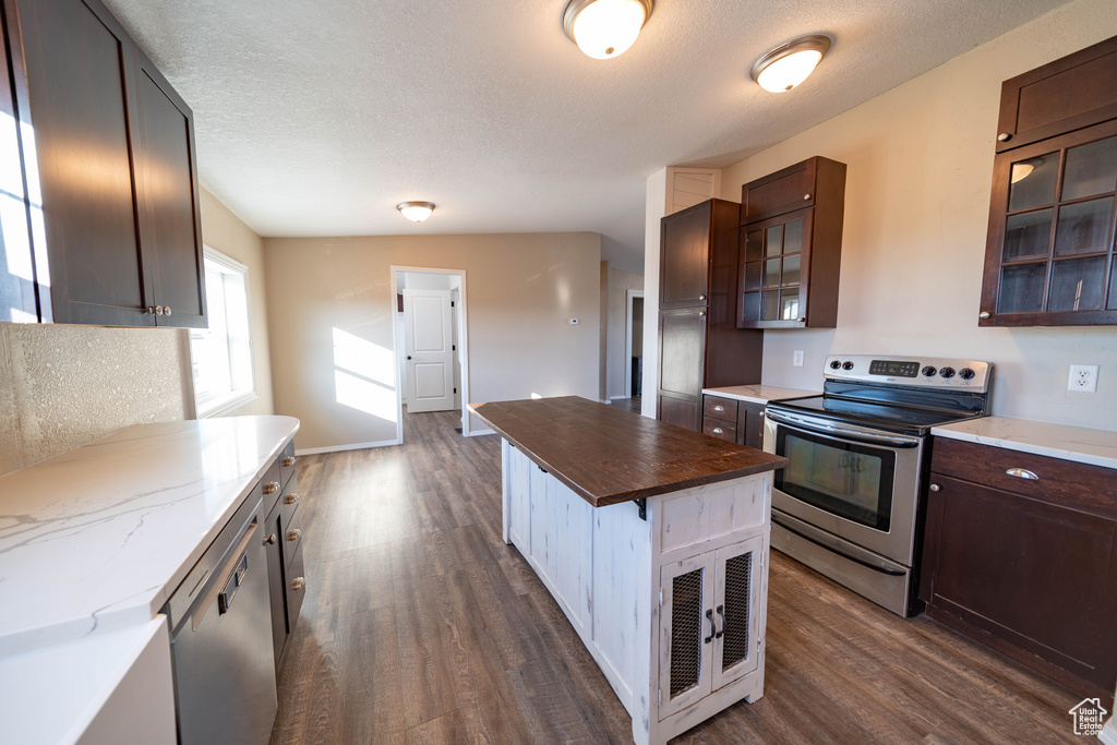 Kitchen featuring stainless steel appliances, dark wood-type flooring, glass insert cabinets, dark brown cabinets, and a textured ceiling