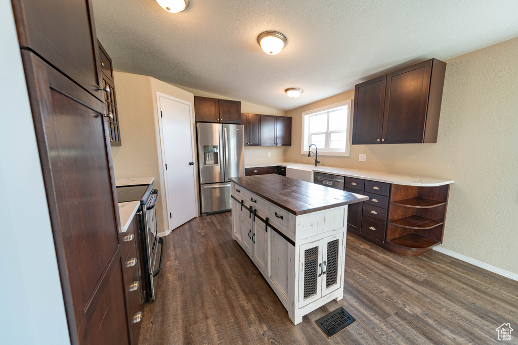 Kitchen with stainless steel appliances, a sink, butcher block counters, dark brown cabinetry, and dark wood-style floors
