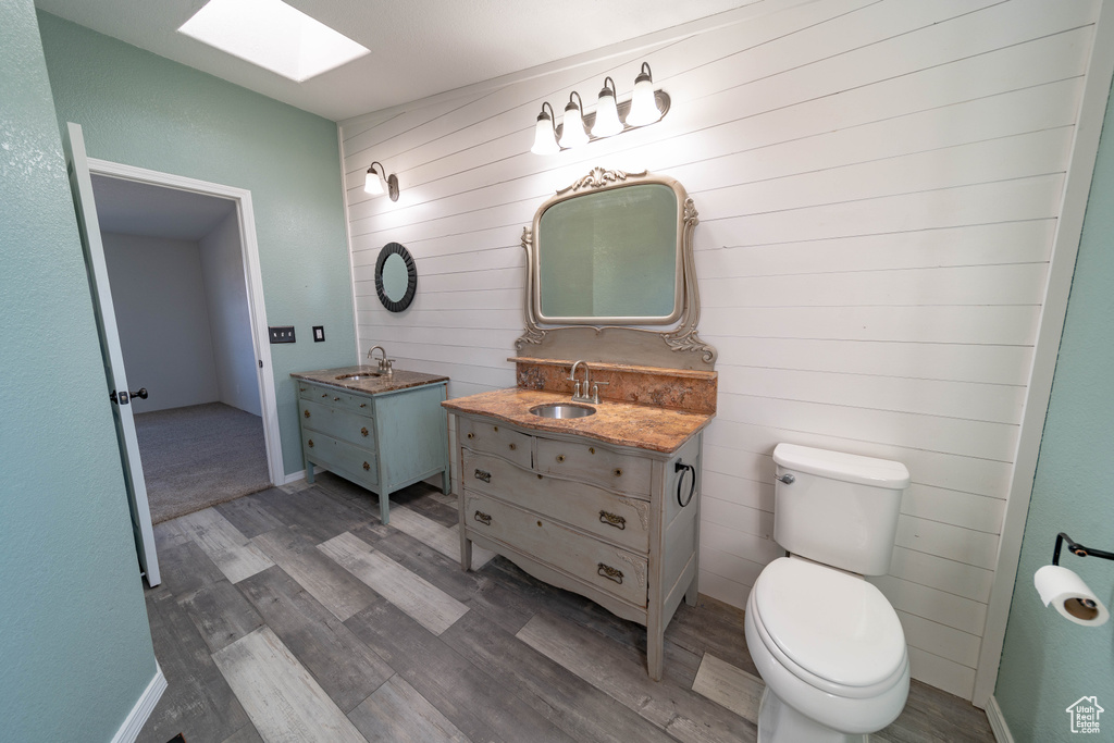 Bathroom featuring a skylight, wood finished floors, two vanities, toilet, and wooden walls