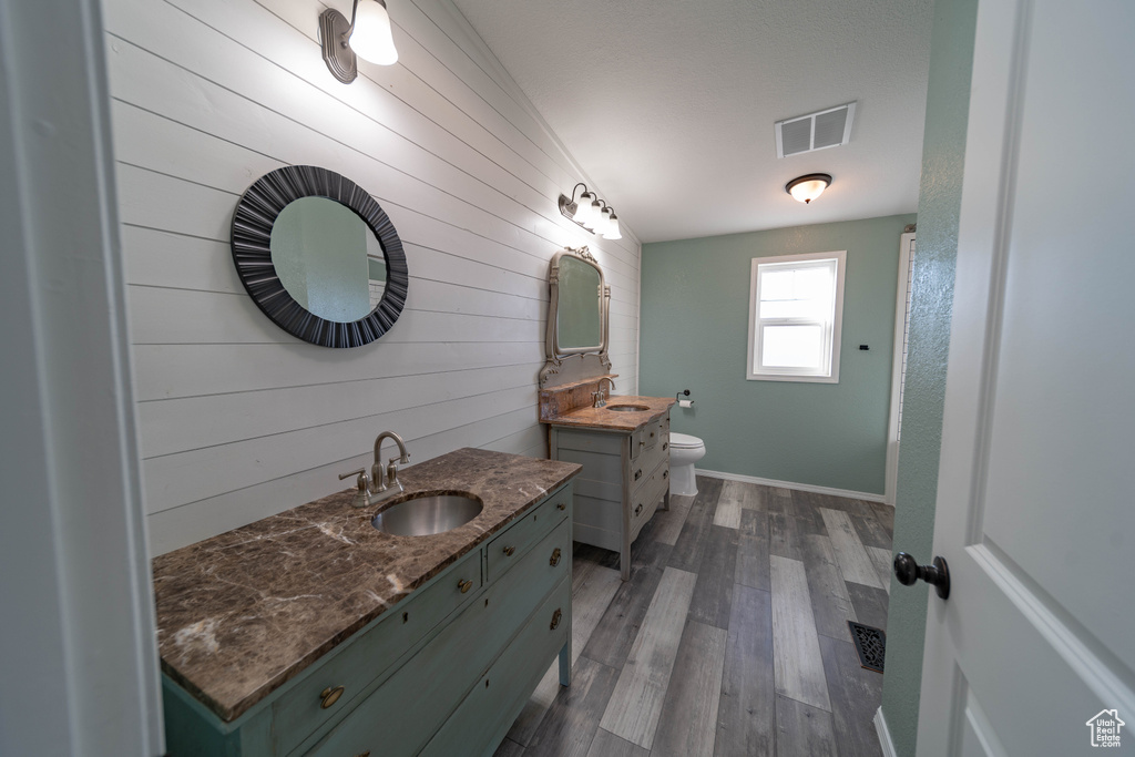 Full bathroom featuring wooden walls, wood finished floors, baseboards, two vanities, and toilet