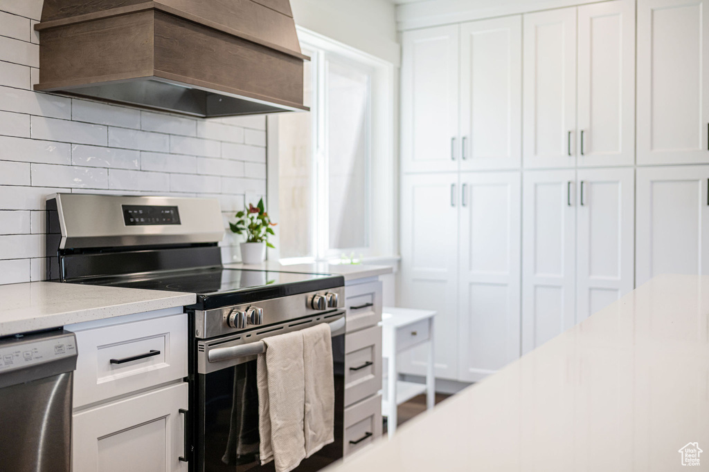 Kitchen with white cabinets, appliances with stainless steel finishes, light stone counters, tasteful backsplash, and custom exhaust hood