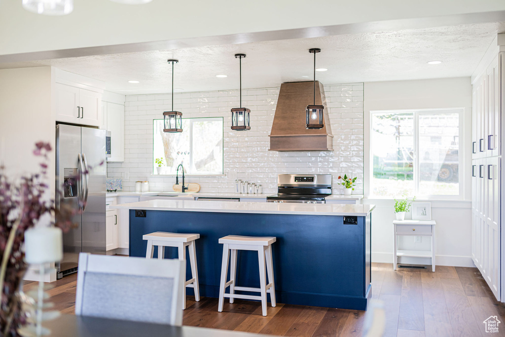 Kitchen featuring custom range hood, light countertops, backsplash, and stainless steel appliances
