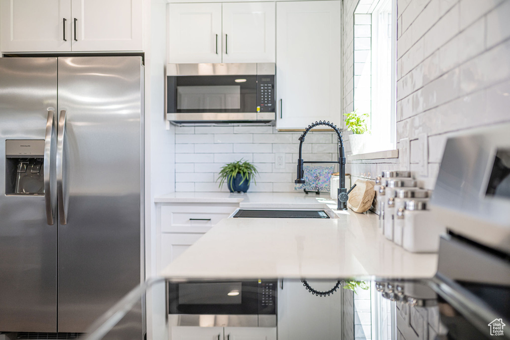 Kitchen with light countertops, white cabinetry, a sink, appliances with stainless steel finishes, and backsplash
