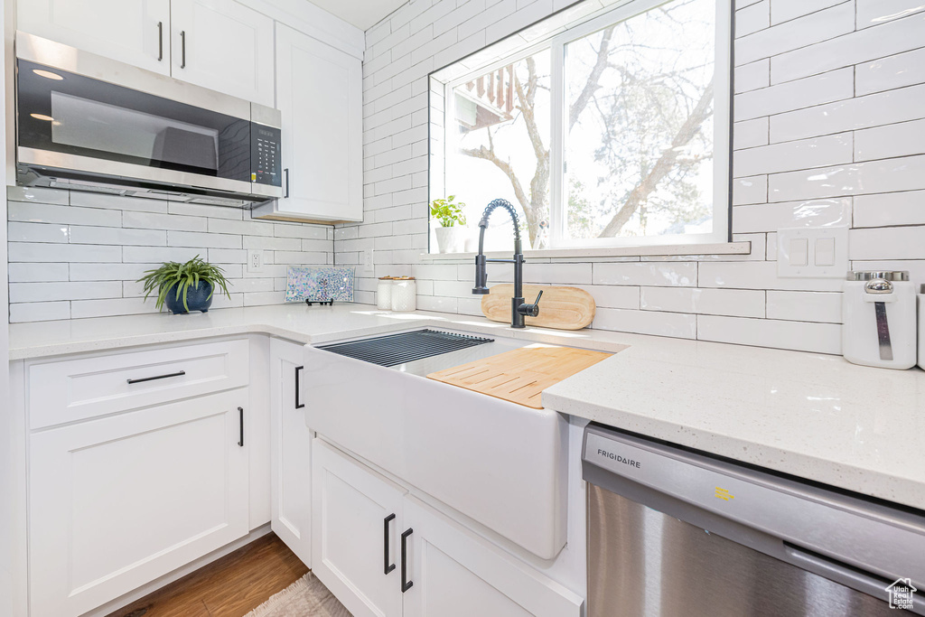 Kitchen with decorative backsplash, light stone countertops, white cabinetry, a sink, and appliances with stainless steel finishes