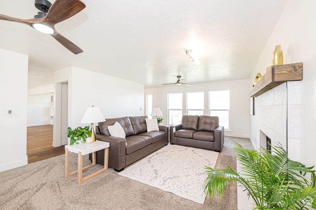 Living room featuring carpet floors, ceiling fan, a tiled fireplace, and baseboards