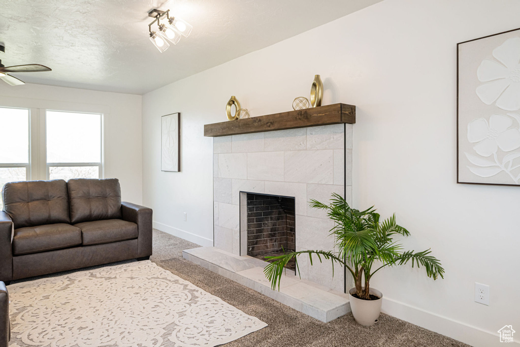 Living room featuring carpet, baseboards, a ceiling fan, and a tile fireplace
