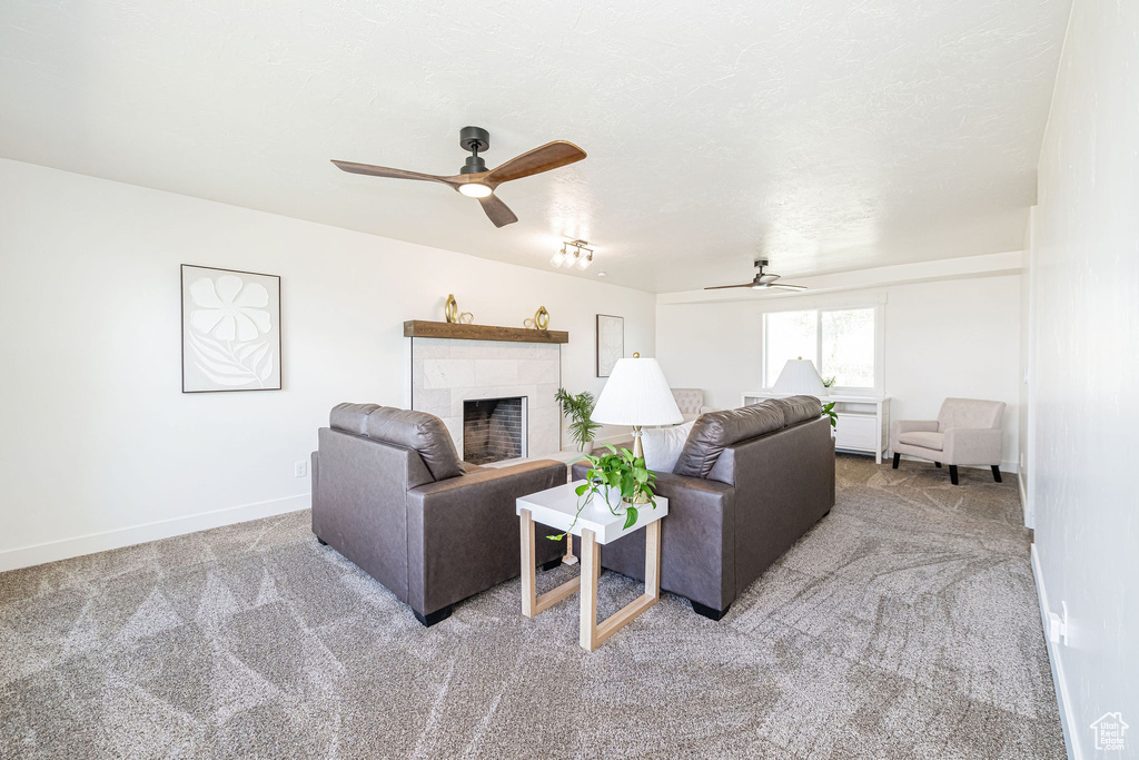 Carpeted living area featuring a ceiling fan, baseboards, and a tiled fireplace