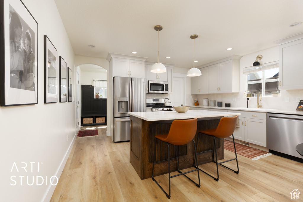 Kitchen with appliances with stainless steel finishes, light wood-type flooring, light countertops, a center island, and a breakfast bar area