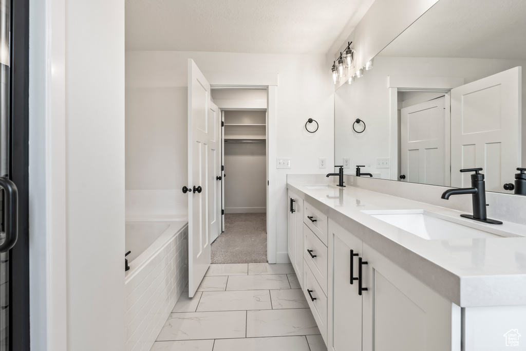 Full bath featuring marble finish floors, tiled tub, double vanity, and baseboards