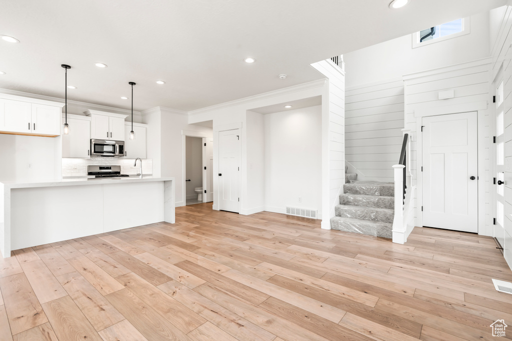 Unfurnished living room with light wood-style floors, a sink, stairs, crown molding, and recessed lighting