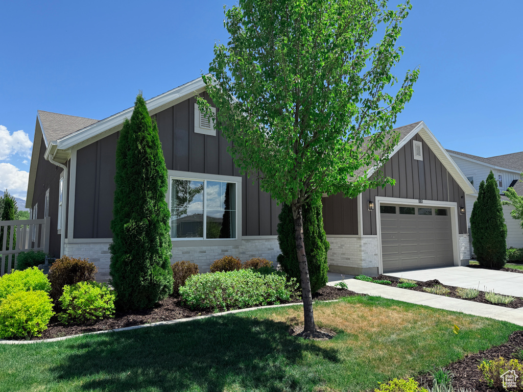 View of front facade featuring board and batten siding, a garage, driveway, brick siding, and a front yard