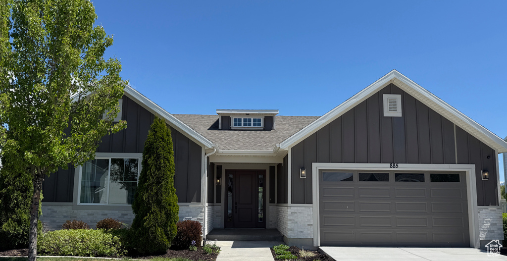 View of front of home with board and batten siding, an attached garage, a shingled roof, and driveway