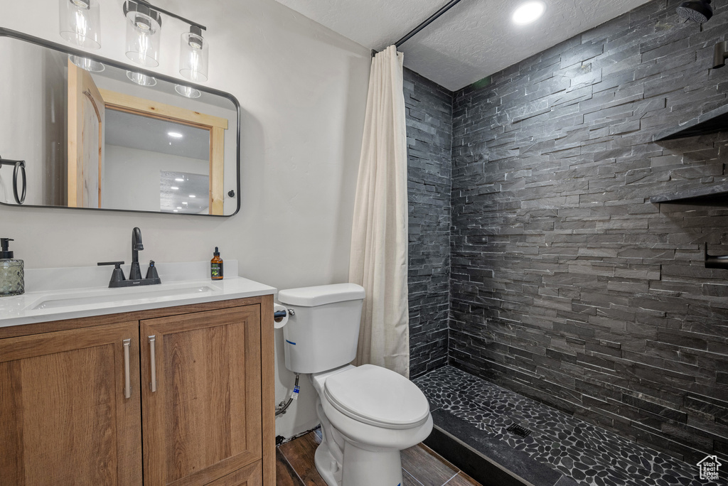 Full bathroom with toilet, tiled shower, vanity, and recessed lighting