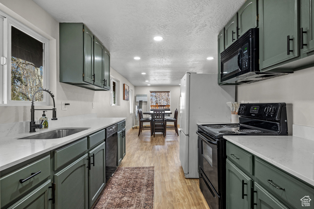Kitchen featuring green cabinetry, black appliances, a sink, recessed lighting, and a textured ceiling