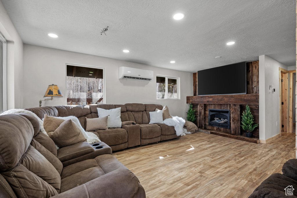 Living room featuring a wall mounted AC, recessed lighting, light wood-style floors, a textured ceiling, and a fireplace with raised hearth