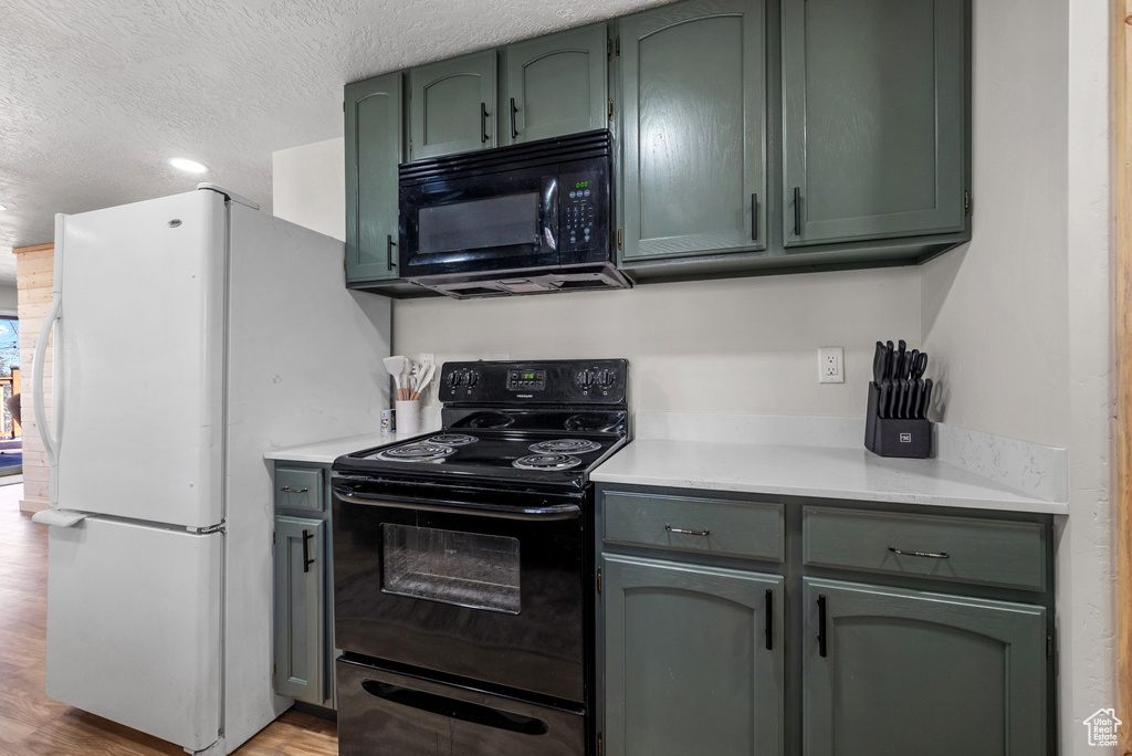 Kitchen featuring black appliances, green cabinets, light countertops, light wood-type flooring, and a textured ceiling