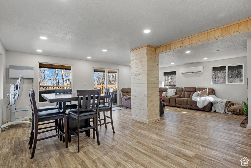Dining space with a textured ceiling, a wall mounted air conditioner, recessed lighting, light wood finished floors, and decorative columns