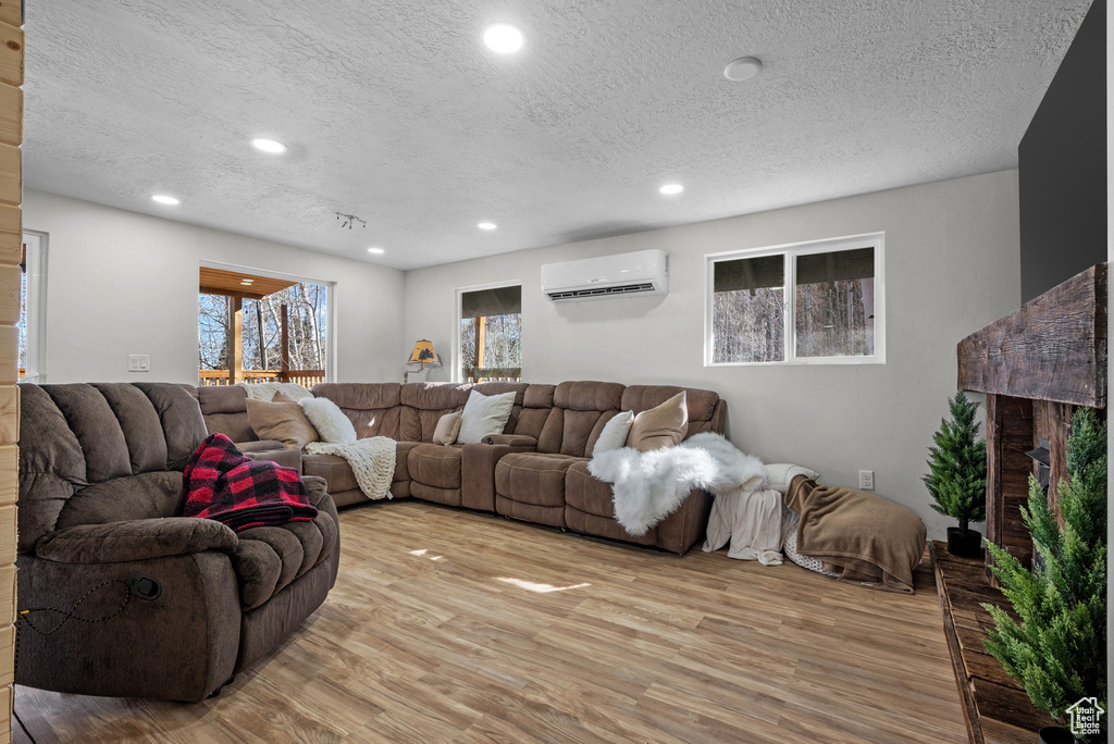 Living room featuring a wall mounted AC, light wood-style floors, a textured ceiling, and recessed lighting