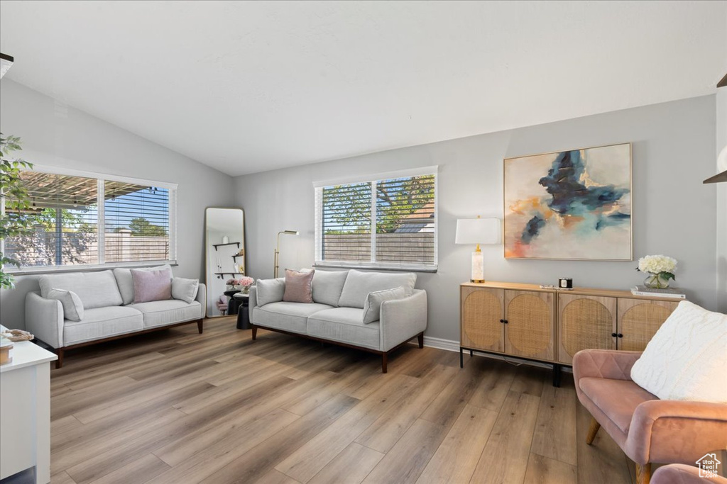Living area featuring light wood-style floors, healthy amount of natural light, vaulted ceiling, and baseboards